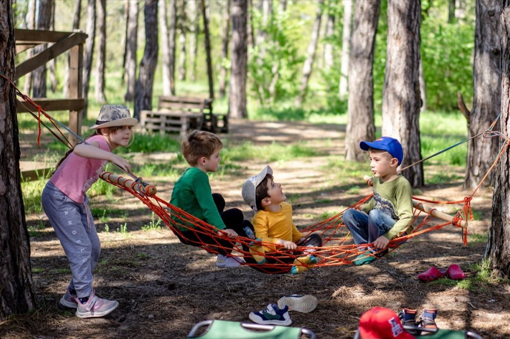 Four children playing together around a rope hammock in the woods
