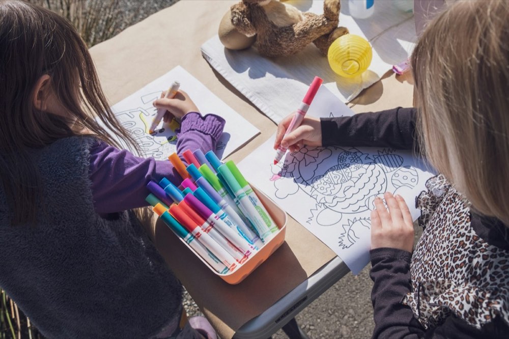 Two girls coloring pages with markers at a table