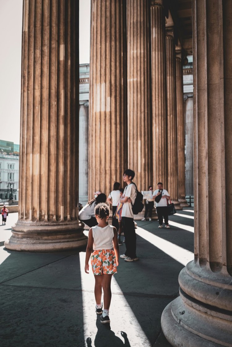 A little girl walking between tall stone columns at a museum